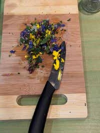 Gehackte blaue und gelbe Blüten liegen mit einem Messer auf einem Schneidebrett.