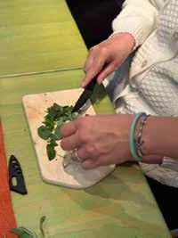 Hände hacken frische grüne Kräuter mit einem Messer auf einem Holzbrett.
