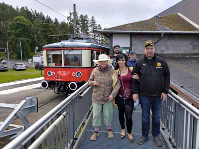 Drei Ausflügler stehen auf einer Brücke vor einem historischen rot-cremefarbenen Triebwagen.