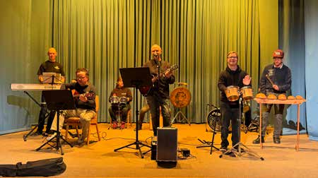 Der Instrumentalkreis spielt auf der Bühne vor einem grünen Vorhang, mit Keyboard, Gitarre, Trommeln und Xylofon.