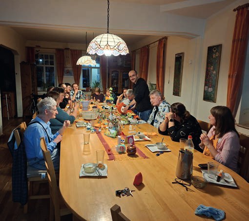 Bewohnerinnen, Bewohner und Mitarbeitende sitzen abends an einem langen Holztisch unter einer bunten Glaslampe beim gemeinsamen Essen.