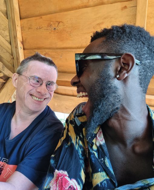 Rahim Ssemambo mit Sonnenbrille lacht gemeinsam mit einem Bewohner mit Brille in die Kamera.